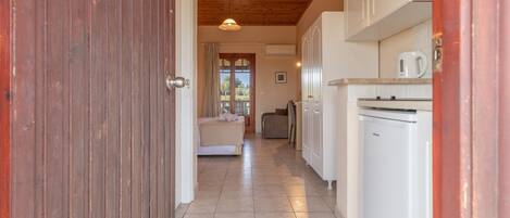 A hallway leading to a bedroom with a wooden ceiling, a kitchen with white cabinets, and a view through a window.