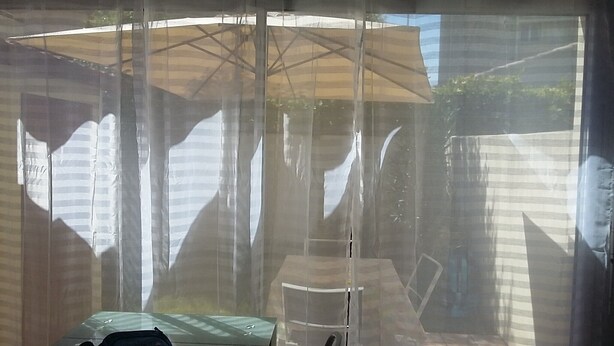 Ein überdachter Patio-Bereich mit Tisch und Stühlen, einem großen Sonnenschirm und Blick auf ein Haus und Bäume.