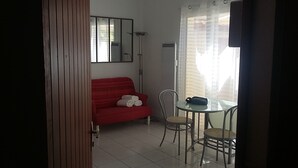 Ein Zimmer mit einem roten Sofa, einem Glastisch mit Stühlen, einem Spiegel und einem Fenster mit Vorhängen.