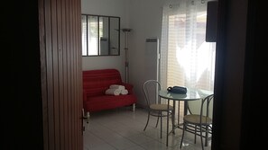 Een kamer met een rode bank, een glazen tafel met stoelen, een spiegel en een raam met gordijnen.