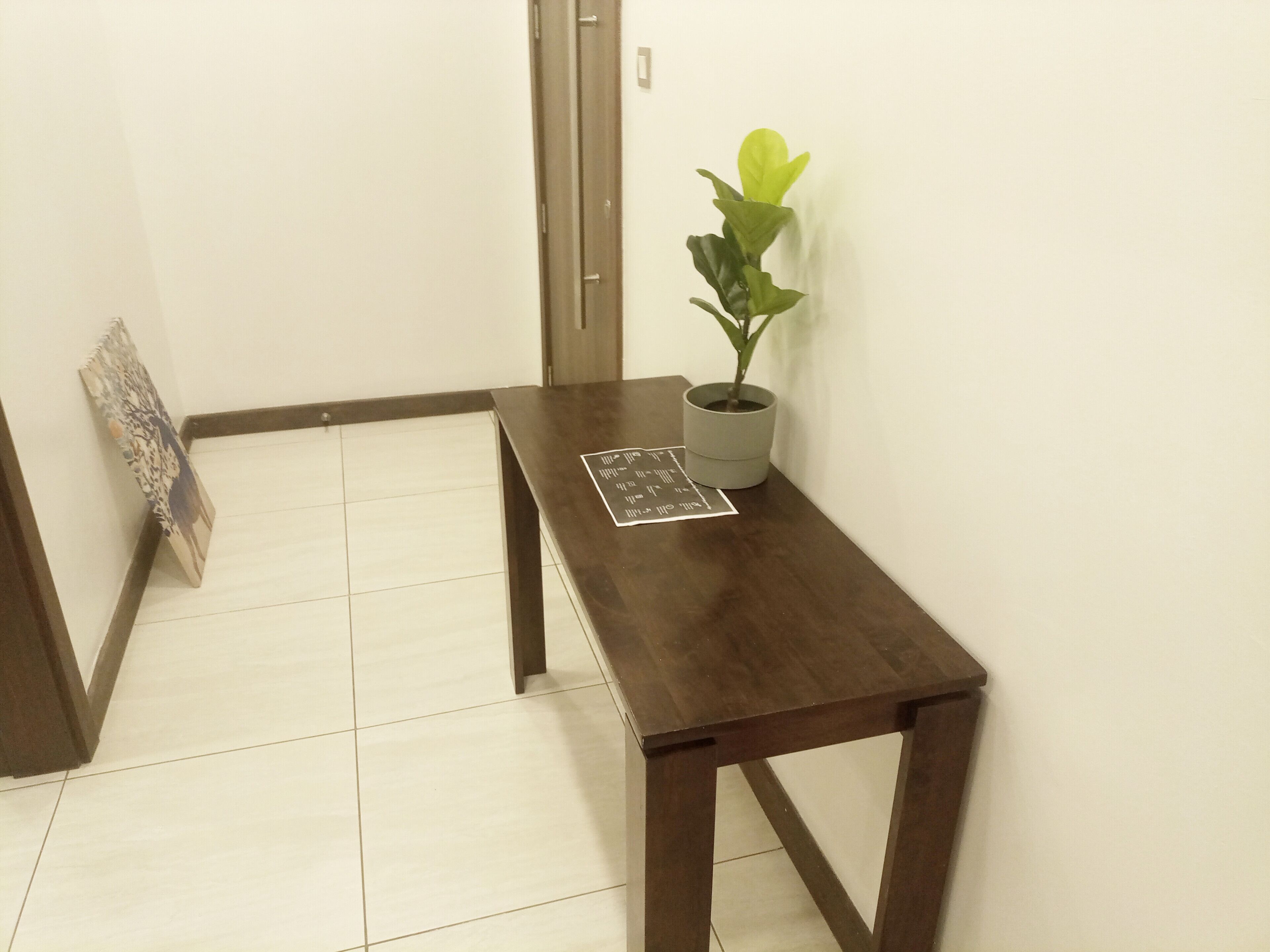 A small wooden table with a potted plant and a framed picture leaning against the wall.