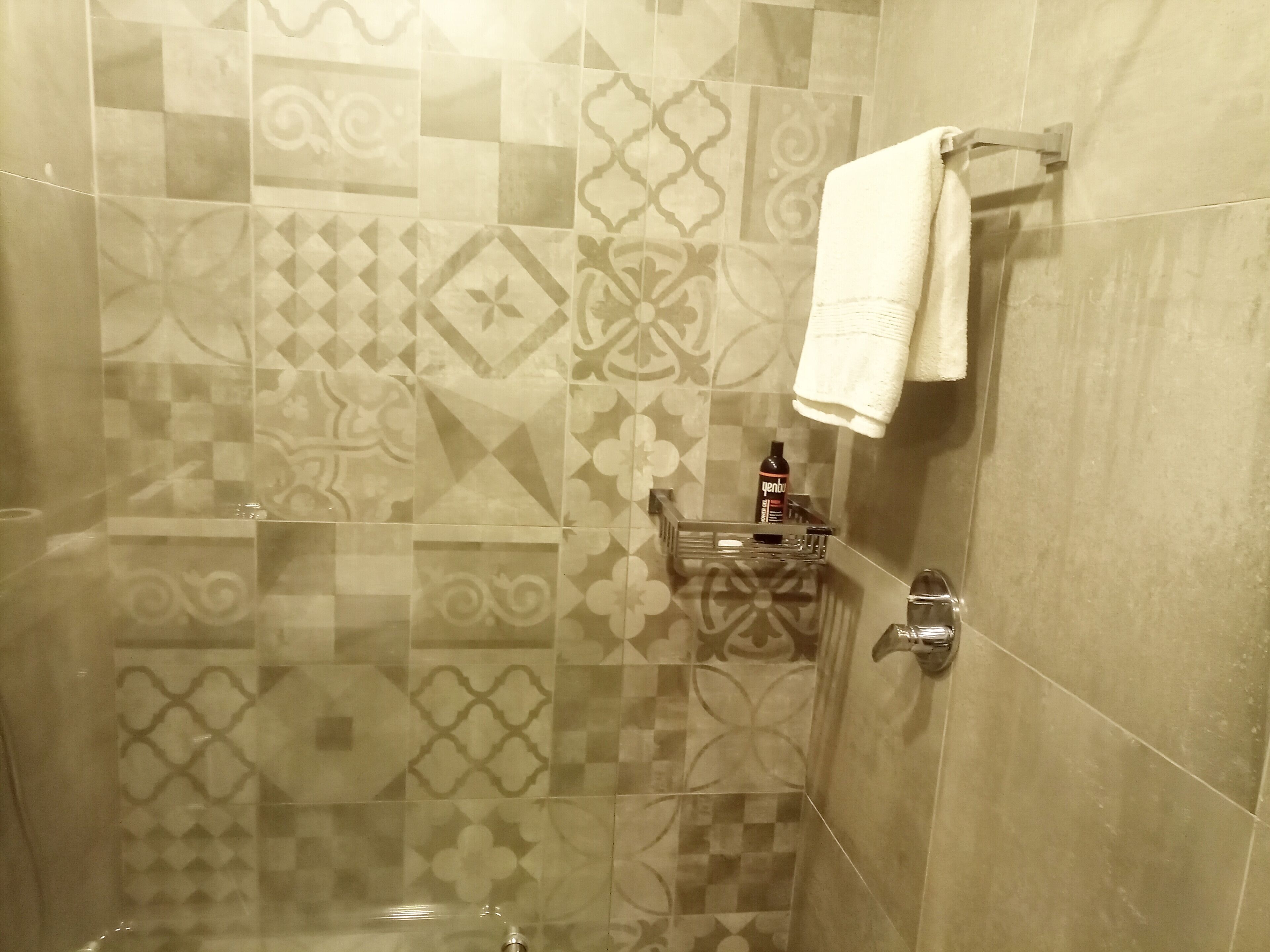A bathroom with patterned tiles, a towel rack, a soap dispenser, and a shower control.