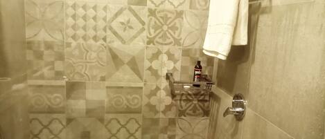 A bathroom with patterned tiles, a towel rack, a soap dispenser, and a shower control.