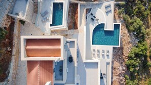 An aerial view of a modern resort with multiple swimming pools, outdoor seating areas, and a terraced pool.