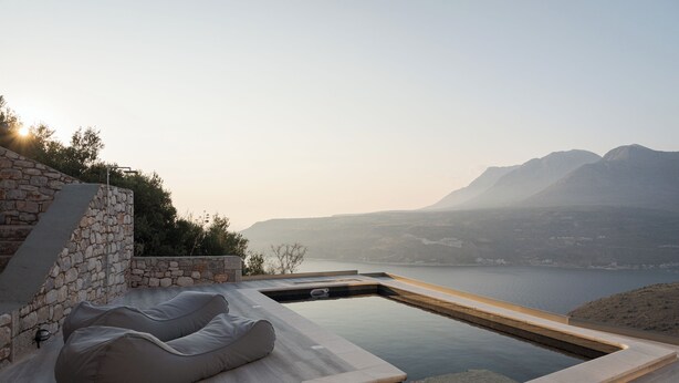 A modern outdoor pool area with stone walls and a view of mountains and a lake.