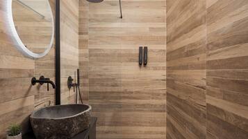 Un baño moderno con pared de madera, un espejo redondo, lavamanos de piedra y ducha con cabezal de ducha manual.