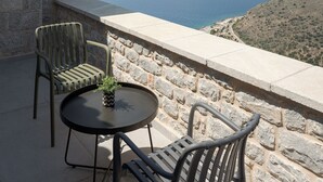 A balcony with stone walls, two chairs, a small round table, and a potted plant.