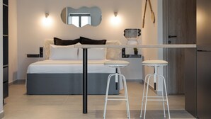 Une chambre moderne avec un lit, deux tabourets de bar blancs, une petite table et un miroir au mur.