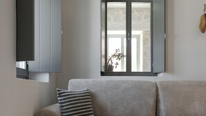 Un salon moderne avec un canapé gris, une petite table d’appoint ronde et blanche, et une fenêtre donnant sur l’extérieur.