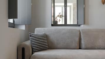 A modern living room with a grey sofa, a round white side table, and a window with a view of the outside.