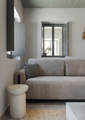 Un salon moderne avec un canapé gris, une petite table d’appoint ronde et blanche, et une fenêtre donnant sur l’extérieur.