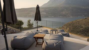 A terrace with outdoor seating, a table, and a view of a lake and mountains.
