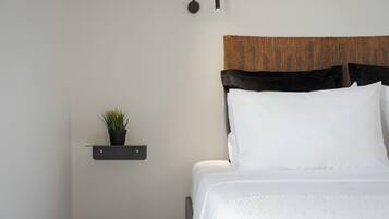 A neatly made bed with a headboard, a small shelf with a plant, and a wall-mounted light fixture.