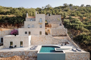 A stone building with a pool, outdoor seating, and a view of the surrounding hills.