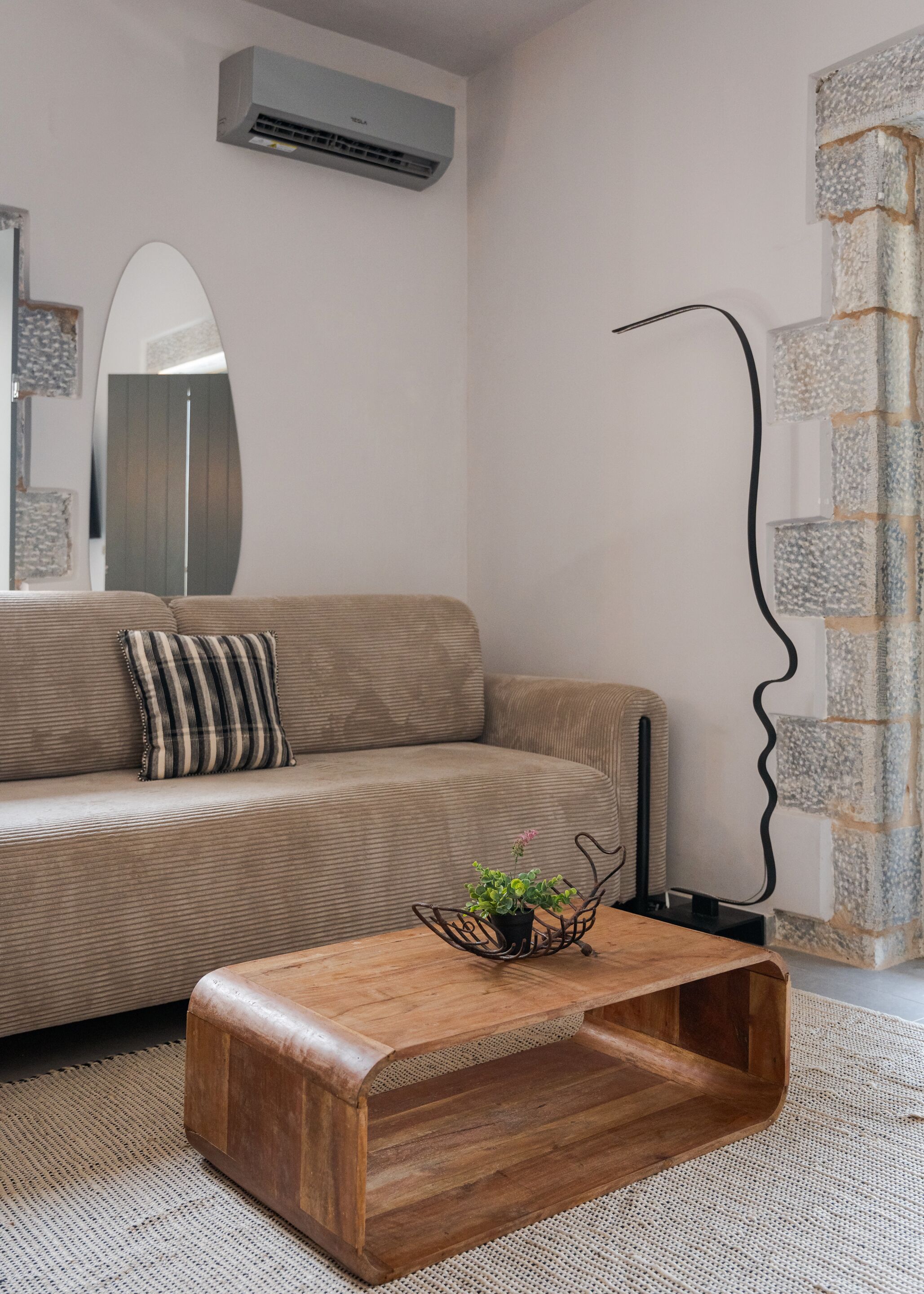 Una sala de estar con un sofá, una mesa de centro de madera, un aire acondicionado instalado en la pared y una decoración de pared original.