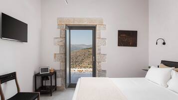 Un dormitorio con cama, escritorio, silla, televisor y puerta que da a un balcón con vistas al paisaje.
