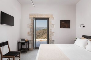 Een slaapkamer met een bed, bureau, stoel, televisie en een deur naar een balkon met uitzicht op het landschap.
