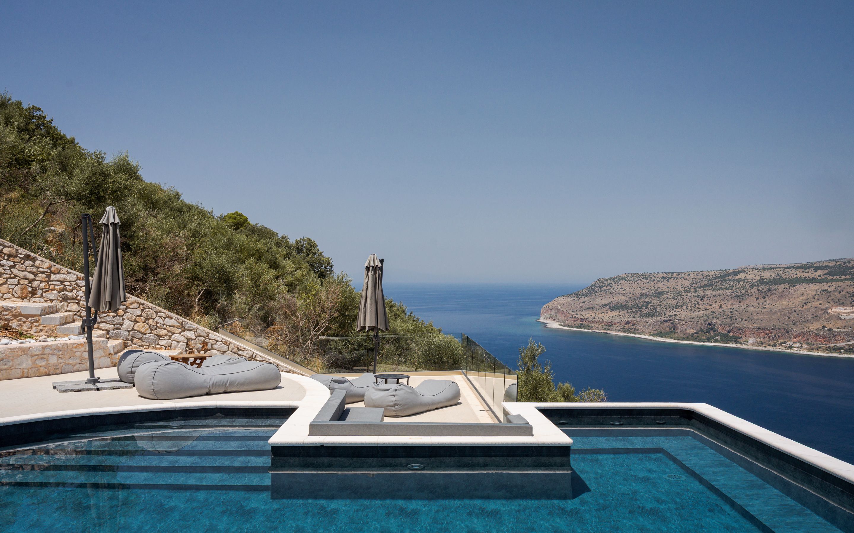 A pool with a view of the sea, stone steps, and outdoor seating.