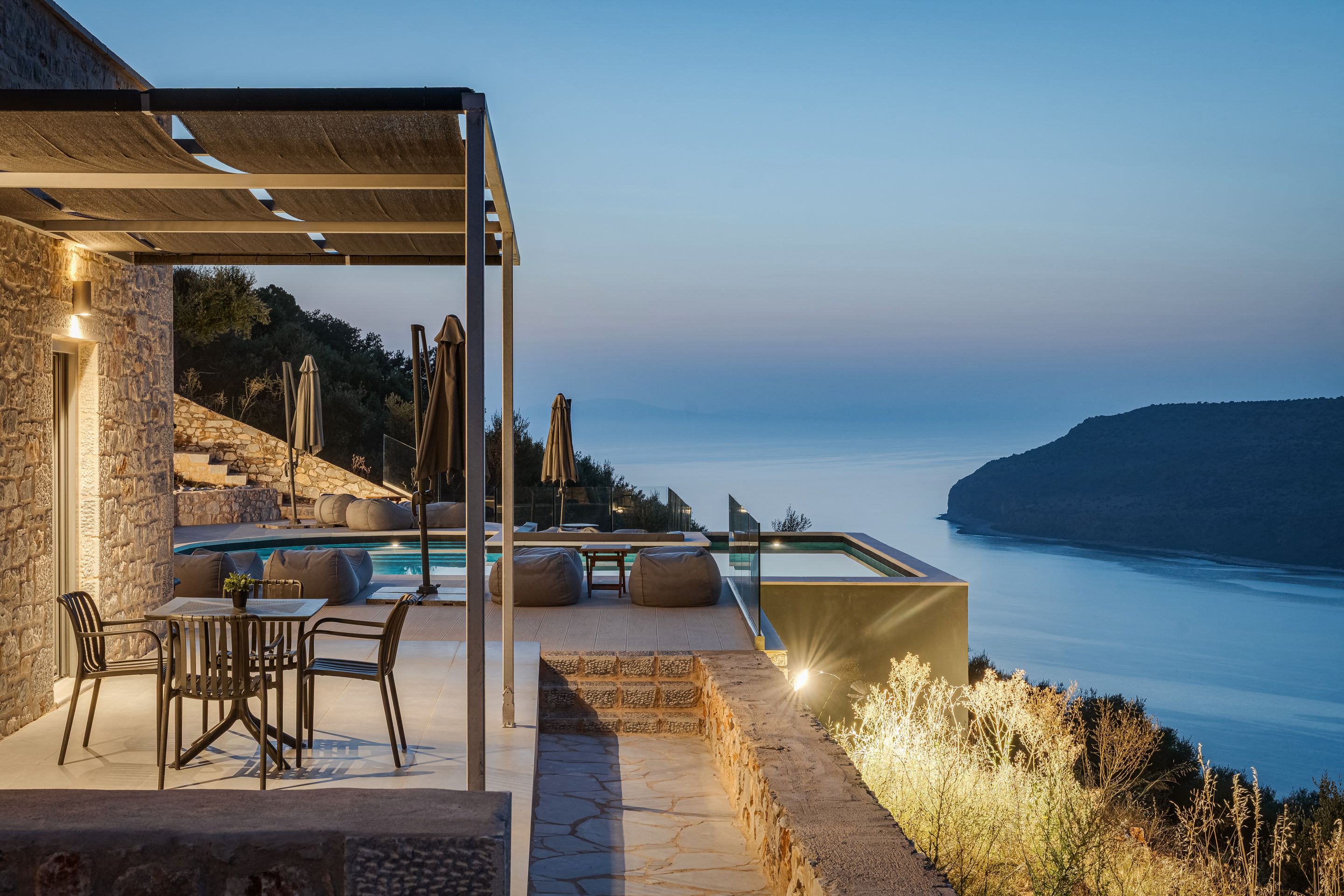 Zona junto a la piscina con mobiliario exterior, vistas al mar y un muro de piedra.