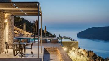 Zona junto a la piscina con mobiliario exterior, vistas al mar y un muro de piedra.