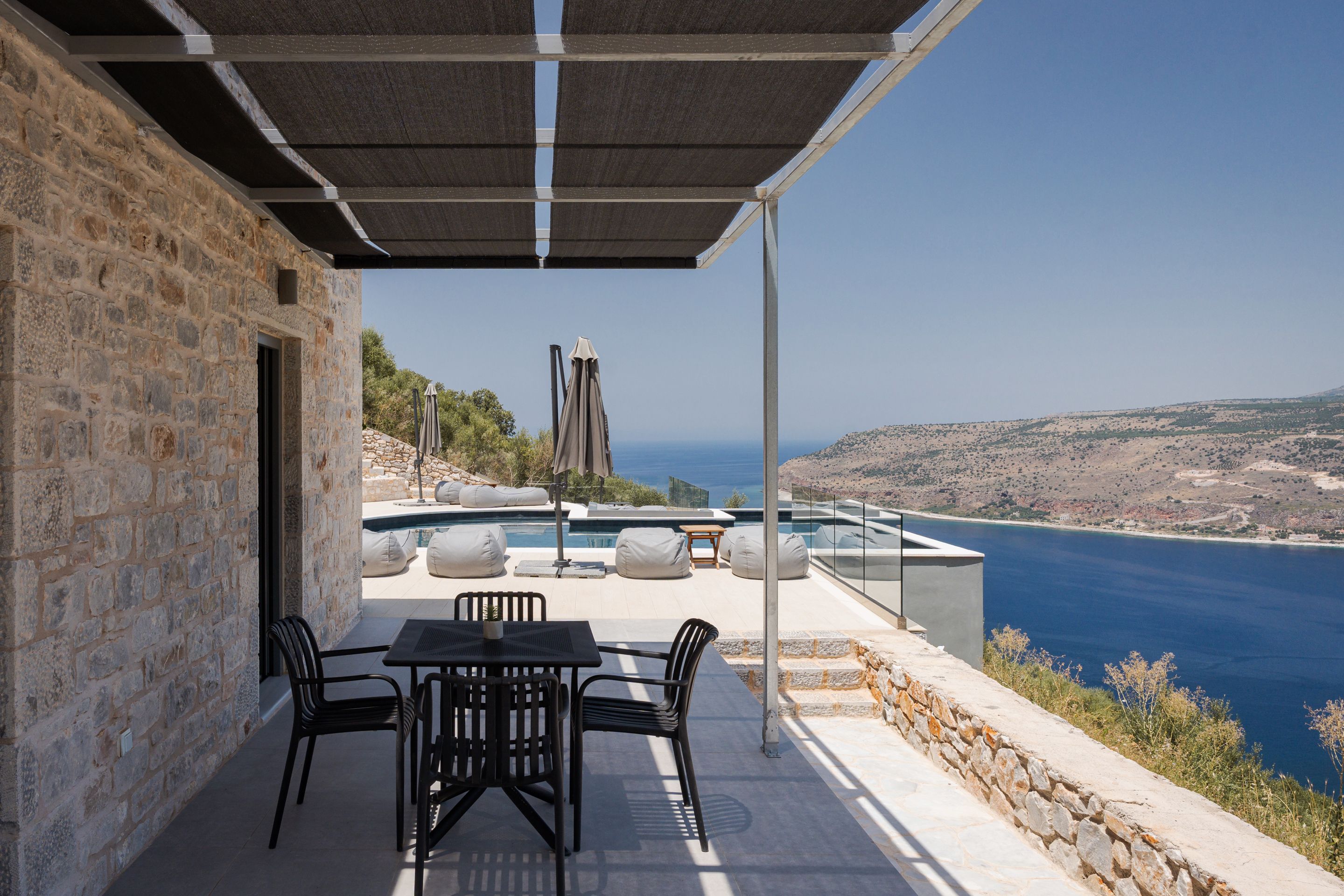 Un patio con mesa y sillas, con vista a una piscina y al mar.