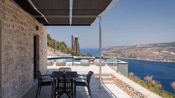 Un patio con mesa y sillas, con vista a una piscina y al mar.
