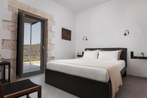 Een slaapkamer met een bed, een stoel, een klein tafeltje, een wandlamp en uitzicht door een glazen deur.