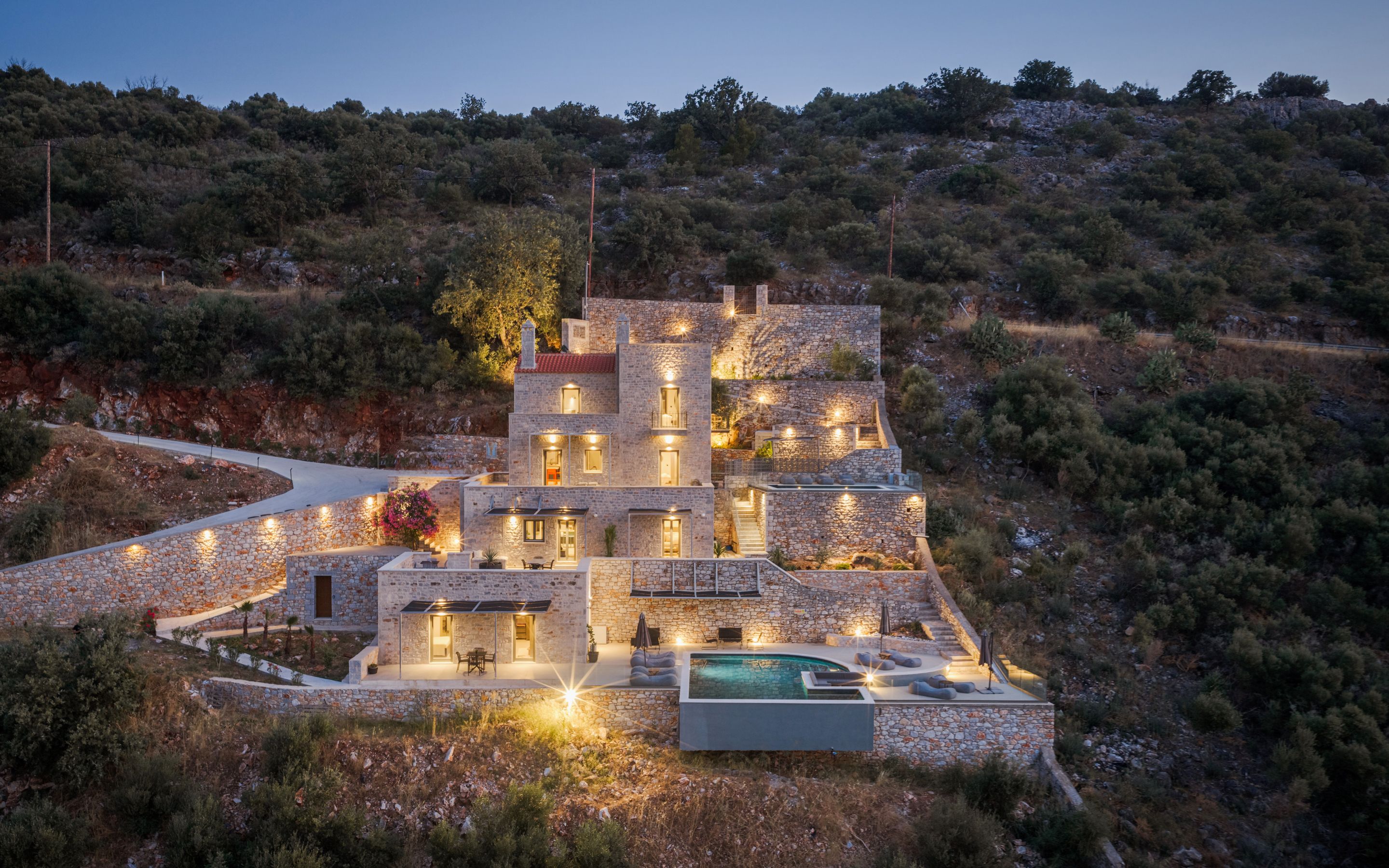 Una villa de piedra con varias habitaciones, piscina y una entrada sinuosa.