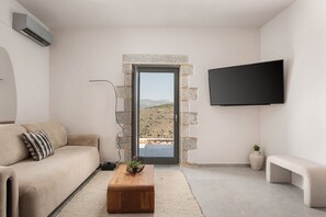 Een moderne woonkamer met een bank, een salontafel, een flatscreen televisie en een stenen deuropstelling die leidt naar een buitenruimte.