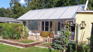 A house with a glass conservatory, a small garden with a wooden fence, and a chimney.
