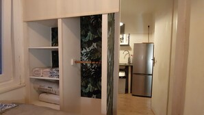 A compact room with a bed, a wardrobe, a small kitchenette, and a door leading to another room.