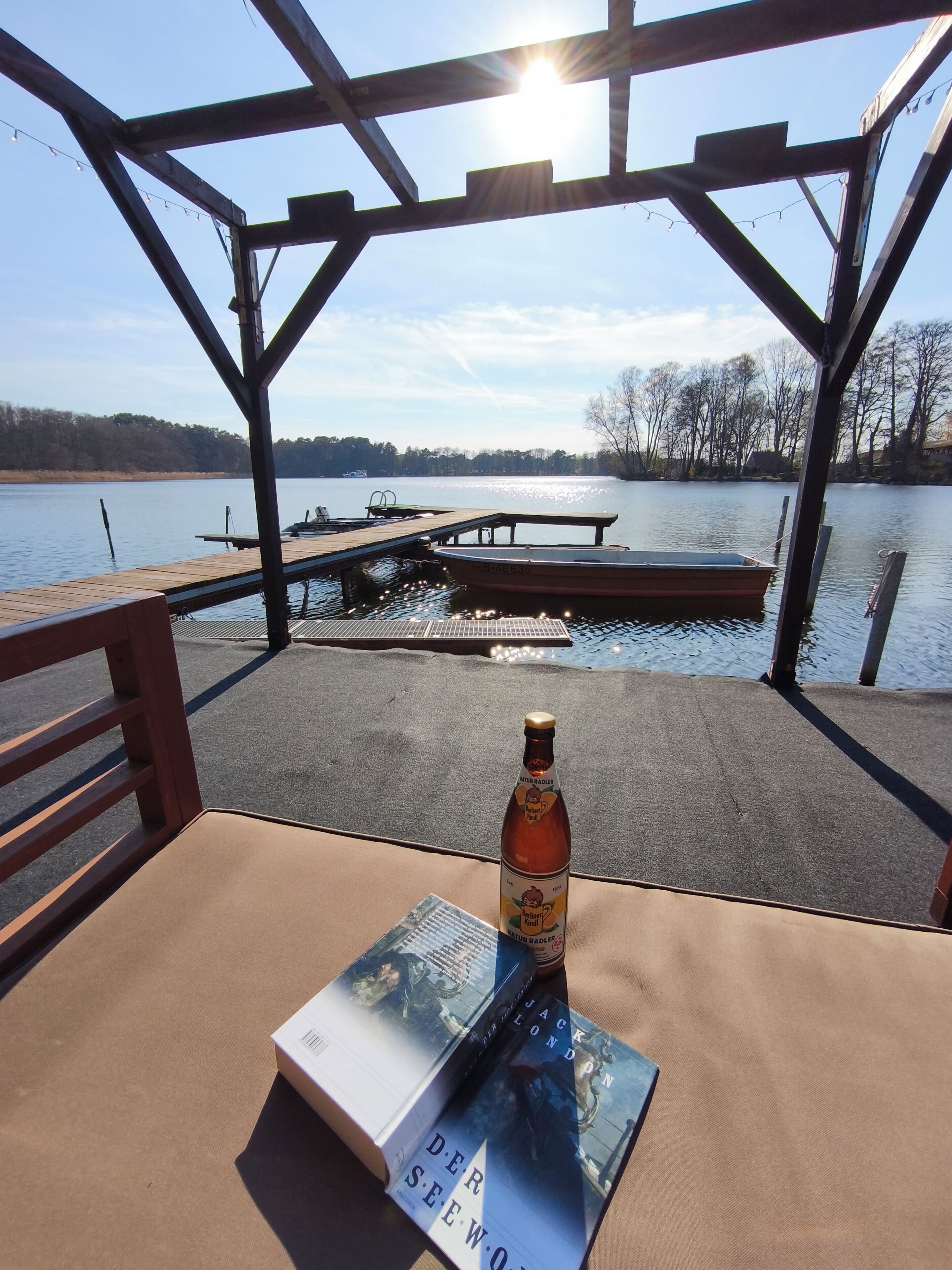A covered outdoor seating area with a view of a lake, a dock, and a boat.