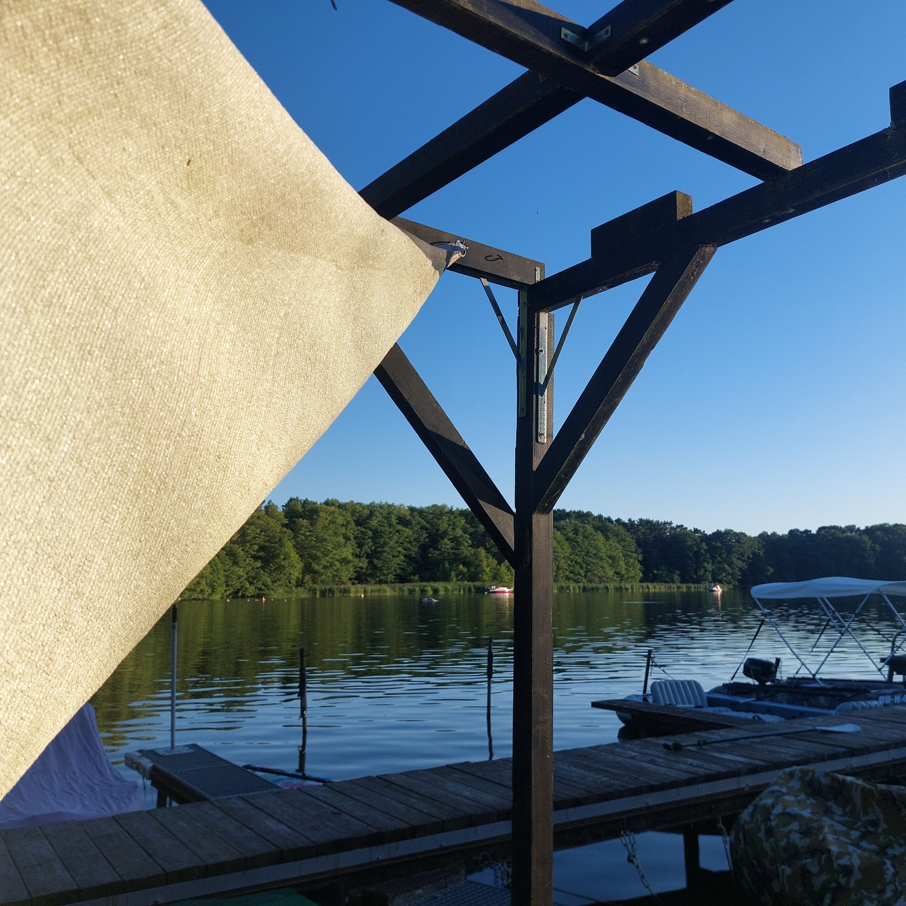 A wooden dock with a boat and a canopy, overlooking a calm lake with a forested shoreline.