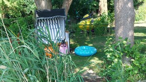 A wooden pathway leading to a striped beach chair and an inflatable pool in a lush garden.