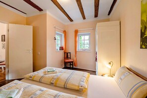 Une chambre avec deux lits, une chaise, une fenêtre avec des rideaux et une lampe de chevet.