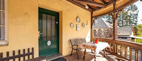 Una terraza de madera con una mesa y sillas, una puerta verde y un pequeño porche.