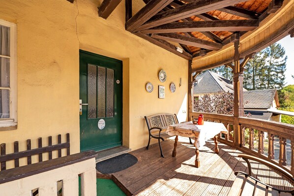 Une terrasse en bois avec une table et des chaises, une porte verte et un petit espace porche.