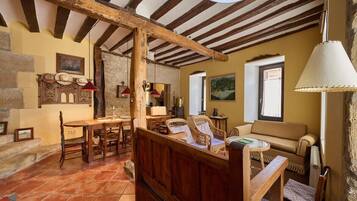 Un interior rústico con vigas de madera a la vista, una pared de piedra, una zona de comedor con muebles de madera y un sofá.