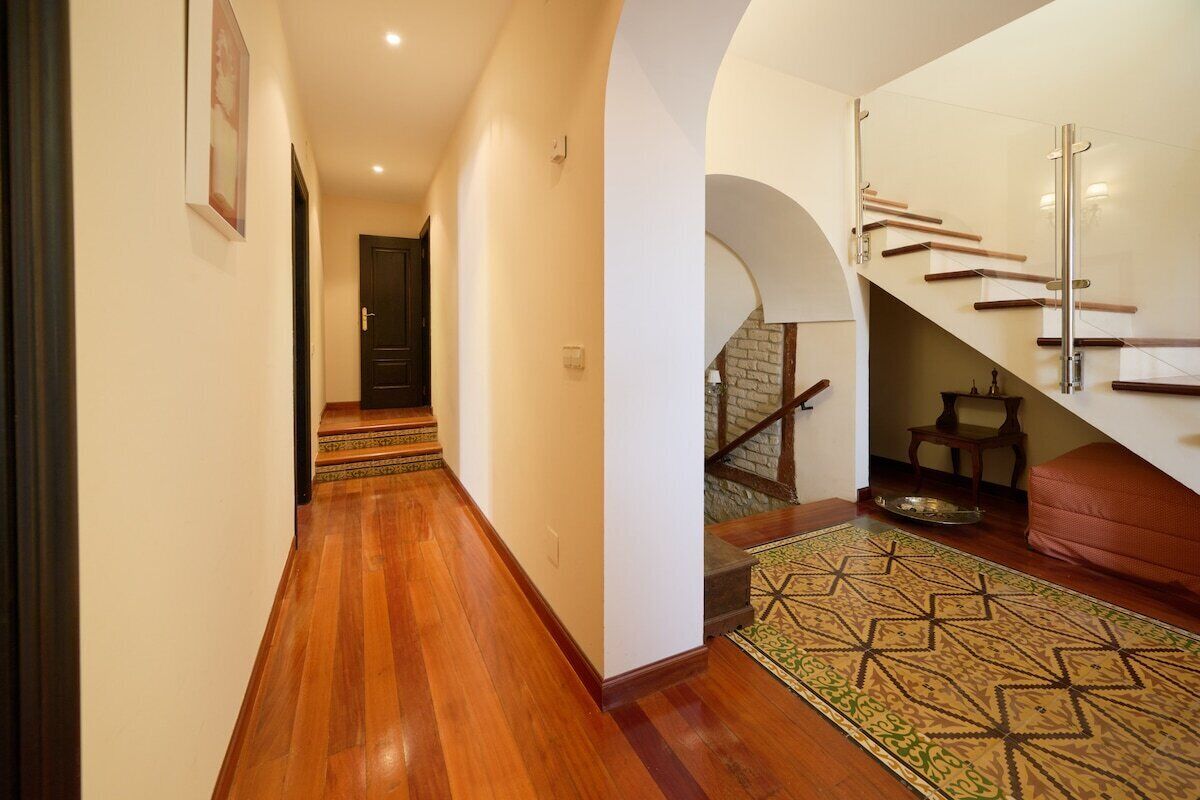 Un couloir doté d’un plancher en bois, d’un escalier avec des rampes en verre et d’un tapis à motifs.