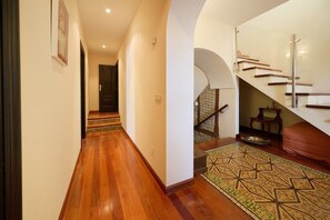 A hallway with wooden flooring, a staircase with glass railings, and a patterned rug.