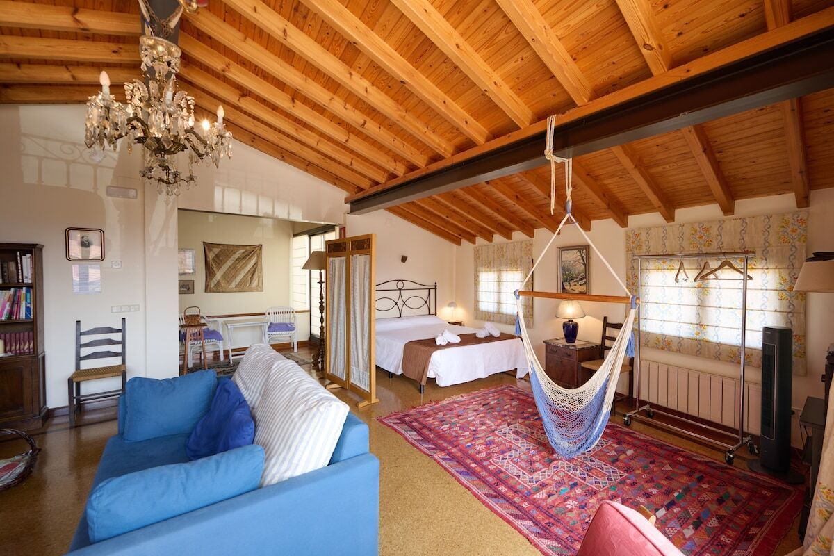 Een kamer met een houten plafond, een hangstoel, een bed, een bank en een kamerbreed tapijt met een patroon.