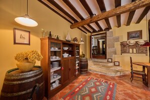 Un intérieur rustique avec des poutres apparentes, un buffet en bois contenant de la vaisselle, un tapis à motifs et un tonneau.