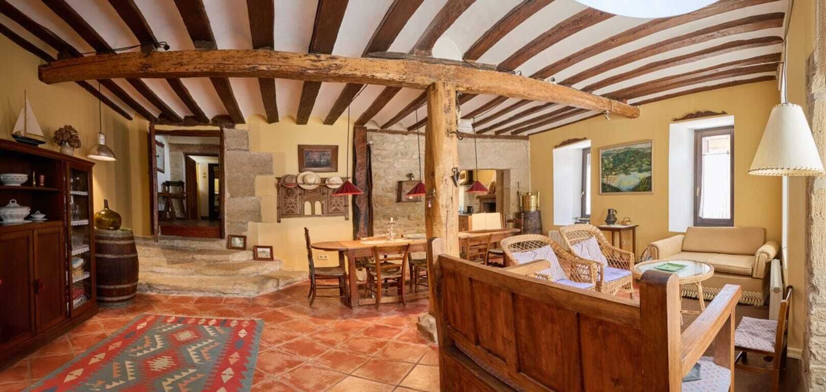 Een rustiek interieur met zichtbare houten balken, een eethoek en een zithoek met een bank en rieten stoelen.