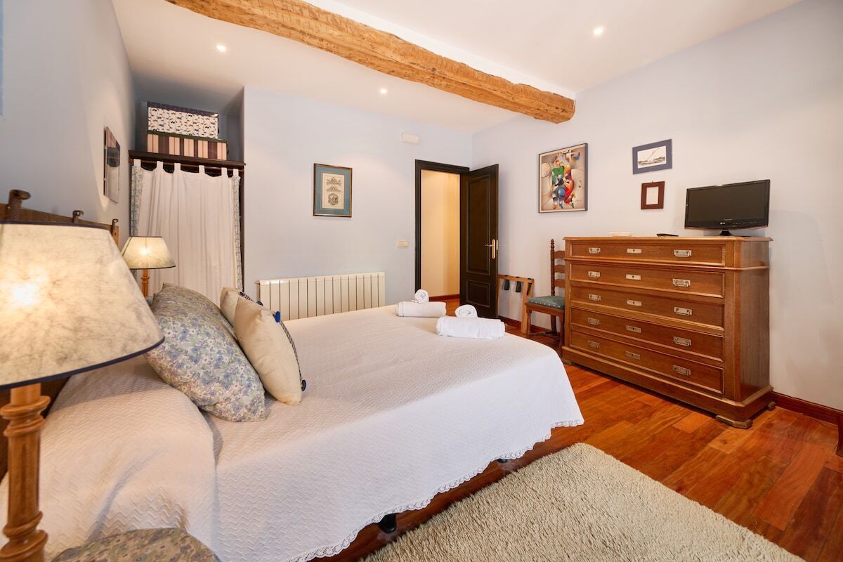 Ein Schlafzimmer mit Bett, Kommode, Fernseher und einer Tür zu einem anderen Raum.