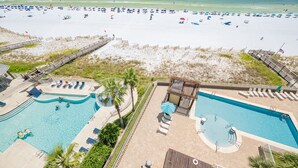Un complexe hôtelier en bord de mer doté d’une piscine, de chaises longues et d’une plage aménagée avec des parasols.