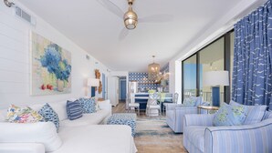 Un salon moderne avec un canapé blanc, des fauteuils à rayures et un coin repas aux couleurs bleu et blanc.