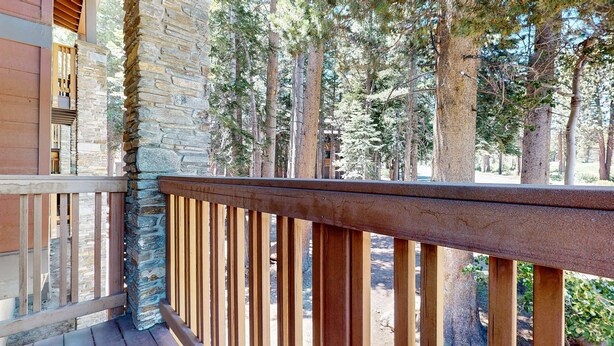 A balcony with a stone wall and wooden railing, overlooking a forested area. - Summit #243 1 Bedroom Condo (Mammoth Lakes)