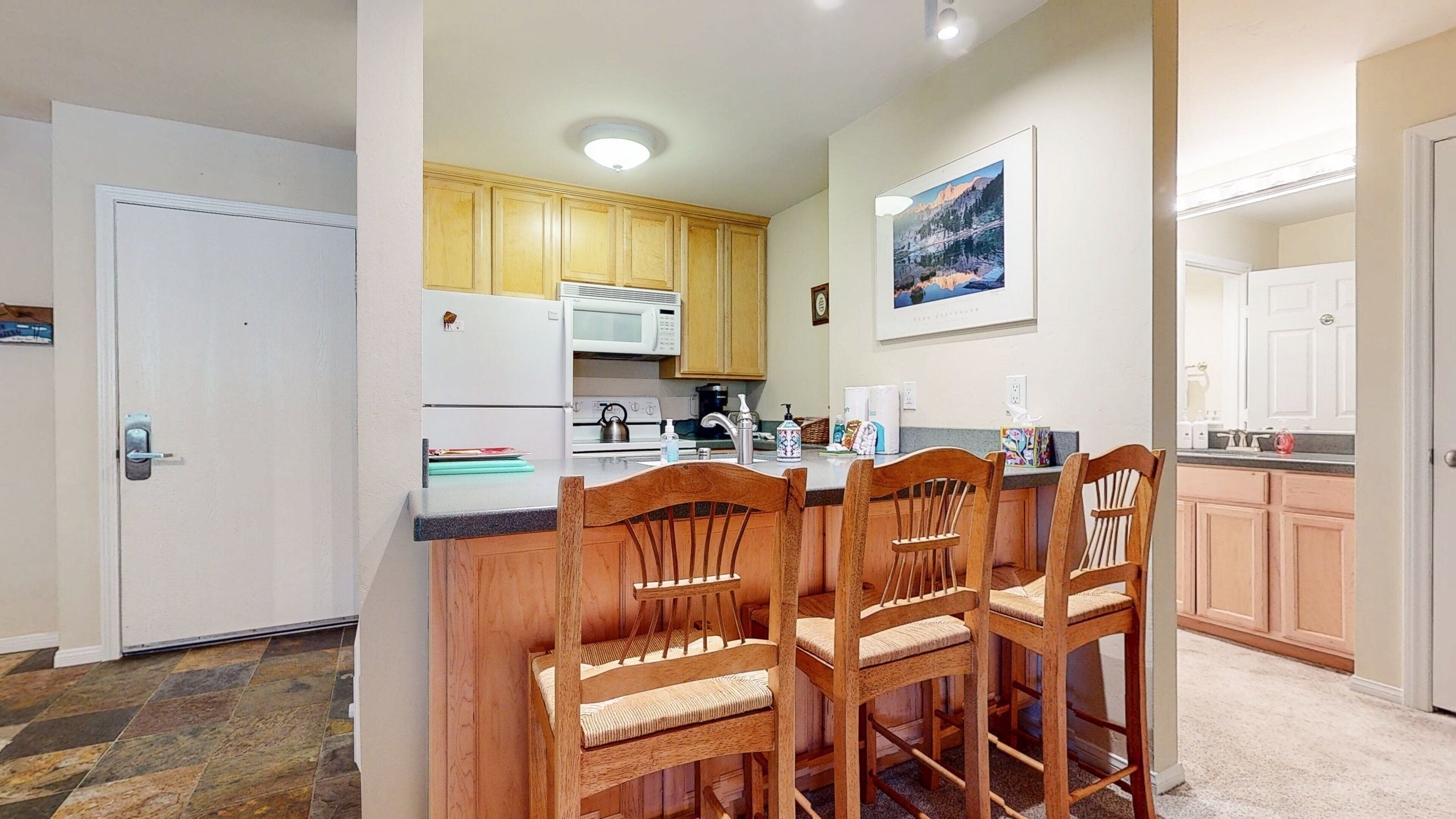 Una cocina compacta con armarios de madera, un refrigerador blanco y una zona de comedor con sillas de madera.