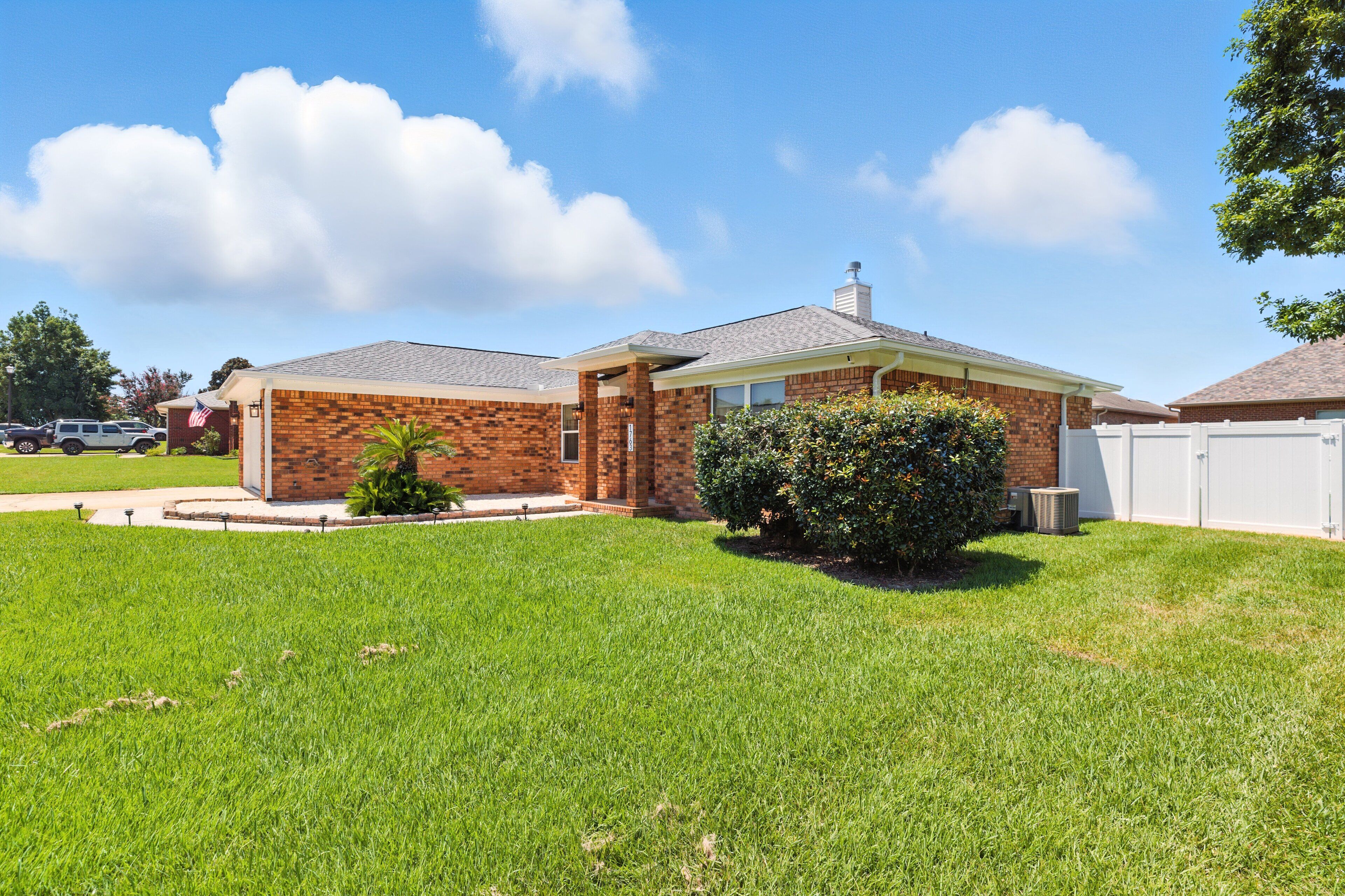 A single-story brick house with a well-maintained lawn, a small garden, and a white garage door.