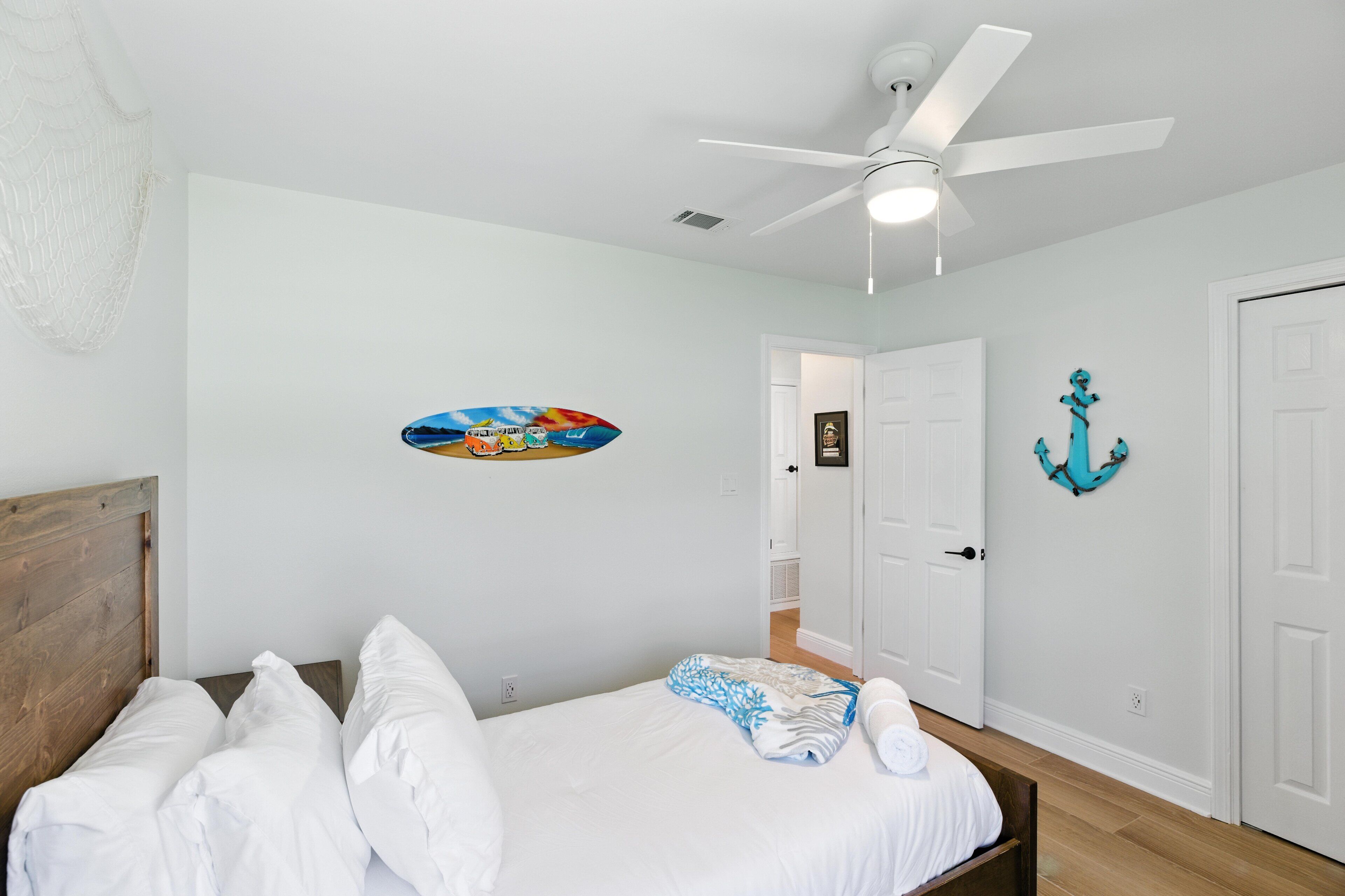 A bedroom with a bed, a ceiling fan, a door, and a wall decoration.